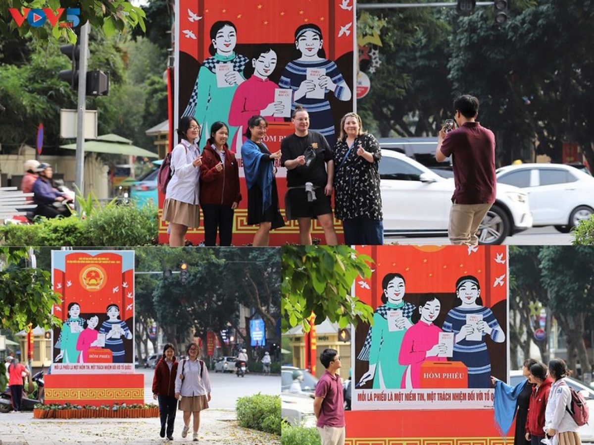 ประชาชนในประเทศและนักท่องเที่ยวต่างชาติร่วมถ่ายภาพเช็คอินอย่างสนุกสนานหน้าป้ายประชาสัมพันธ์วันเลือกตั้งบนถนนบ่าเตรี่ยว แขวงเกื๋อนาม